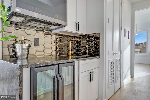 bar with wine cooler, dark stone countertops, tasteful backsplash, and white cabinets