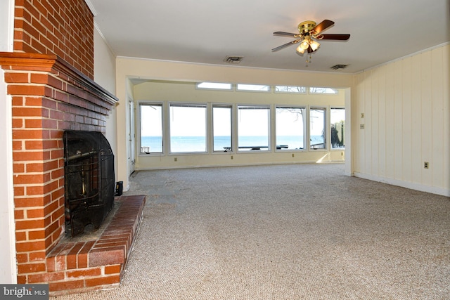 unfurnished living room with ceiling fan, carpet, a water view, ornamental molding, and a brick fireplace