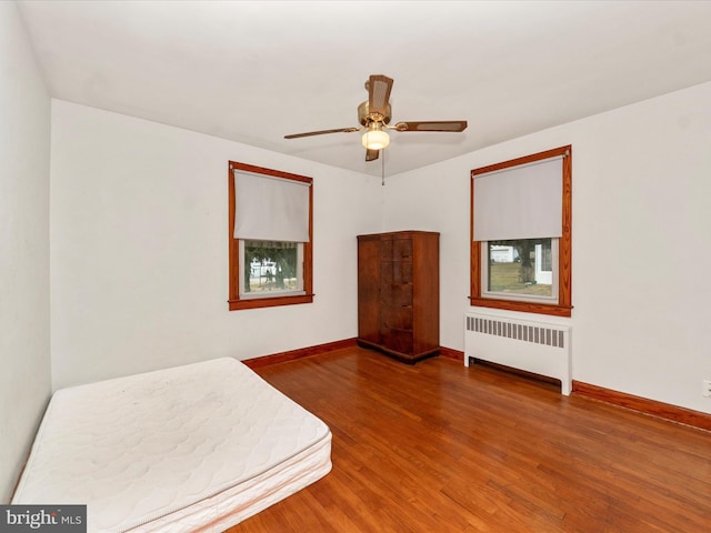 unfurnished bedroom featuring ceiling fan, radiator heating unit, and wood-type flooring