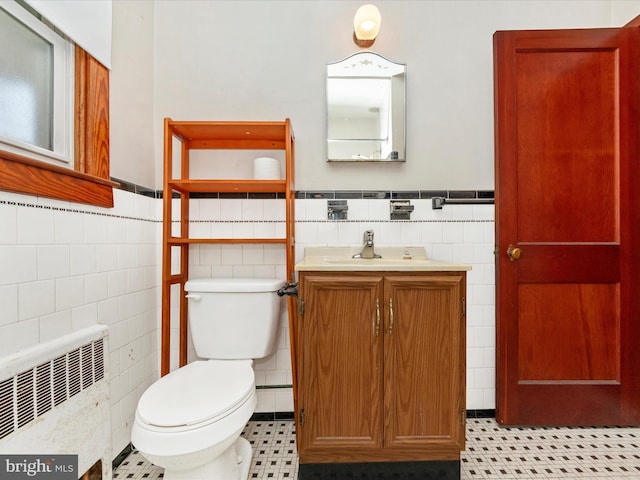 bathroom featuring radiator heating unit, toilet, vanity, and tile walls