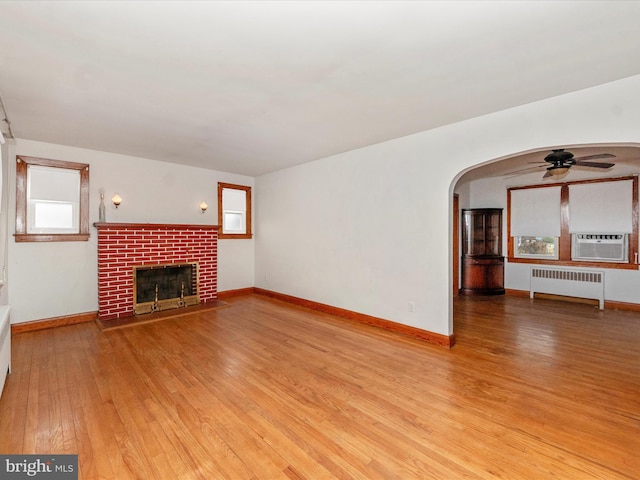 unfurnished living room with radiator, a fireplace, cooling unit, ceiling fan, and light hardwood / wood-style flooring