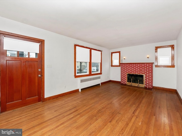 unfurnished living room featuring radiator heating unit, a brick fireplace, and light hardwood / wood-style flooring