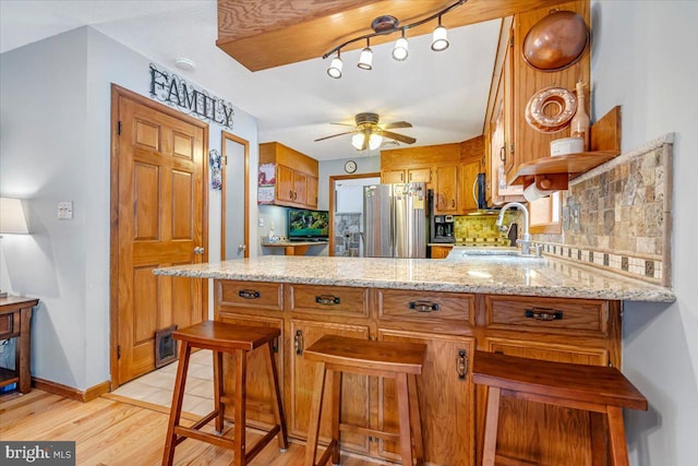 kitchen with a breakfast bar, sink, stainless steel refrigerator, kitchen peninsula, and decorative backsplash