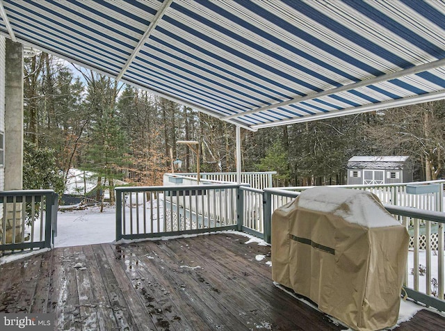 snow covered deck with area for grilling and a shed