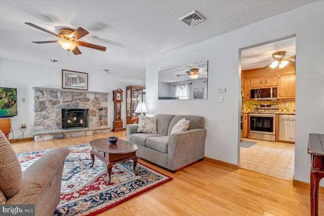 living room with ceiling fan, a textured ceiling, a fireplace, and light hardwood / wood-style flooring