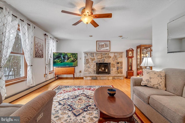 living room featuring a stone fireplace, a baseboard radiator, wood-type flooring, ceiling fan, and a textured ceiling