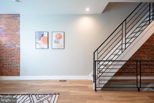 stairs featuring brick wall and wood-type flooring