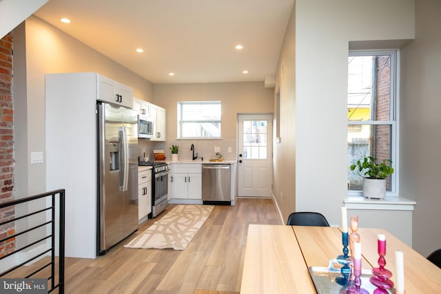 kitchen with sink, white cabinetry, backsplash, stainless steel appliances, and light hardwood / wood-style floors