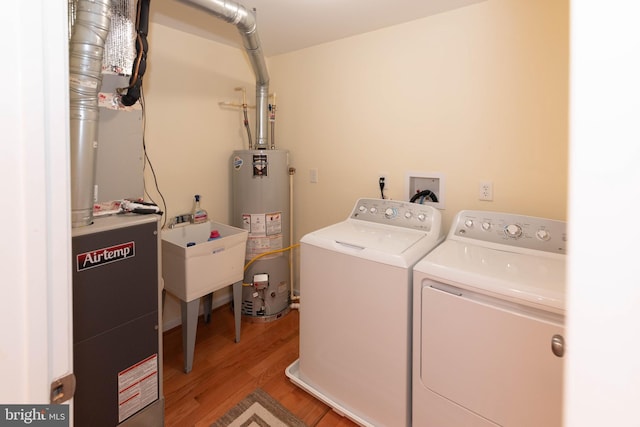 laundry room with washing machine and clothes dryer, sink, water heater, and light wood-type flooring