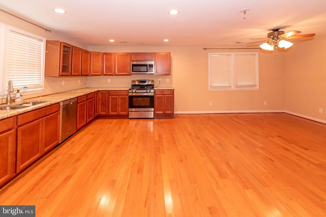 kitchen with appliances with stainless steel finishes, light hardwood / wood-style floors, sink, and light stone countertops