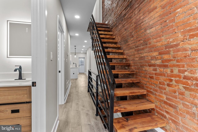 stairs with sink, wood-type flooring, and brick wall