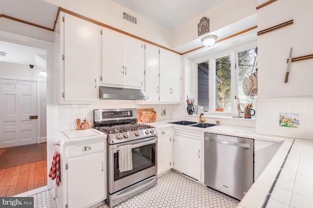 kitchen with visible vents, white cabinets, tile counters, appliances with stainless steel finishes, and under cabinet range hood