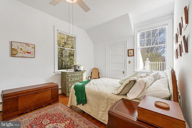 bedroom with light wood-style floors, ceiling fan, a baseboard heating unit, and vaulted ceiling