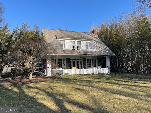 view of front of property with fence, a ceiling fan, stone siding, a front lawn, and a chimney