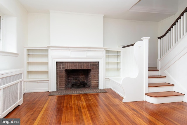 unfurnished living room with wood-type flooring, crown molding, radiator heating unit, and a fireplace