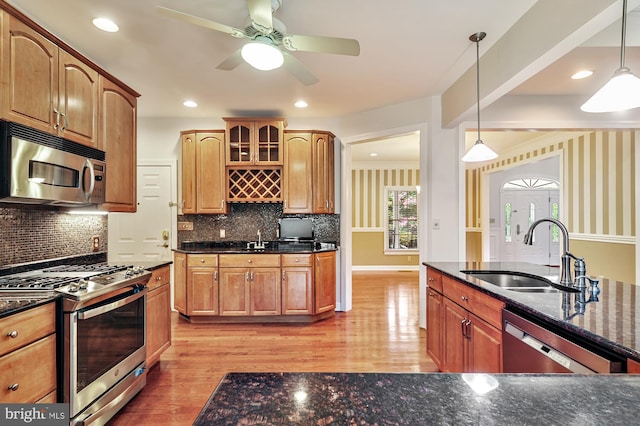 kitchen featuring appliances with stainless steel finishes, sink, backsplash, hanging light fixtures, and light hardwood / wood-style floors