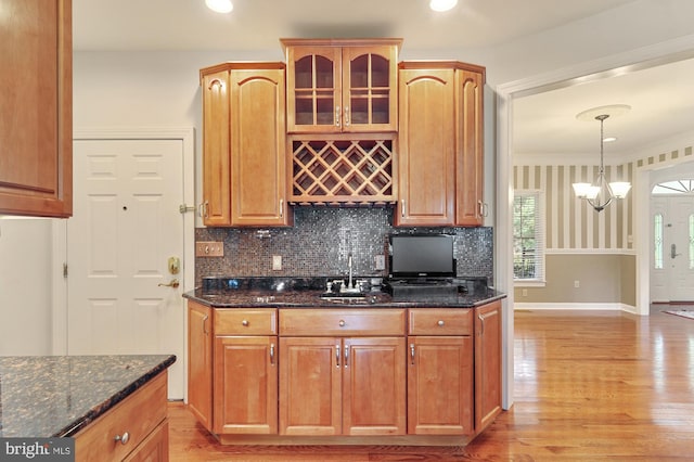 kitchen featuring sink, light hardwood / wood-style flooring, dark stone countertops, hanging light fixtures, and tasteful backsplash