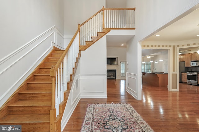 stairway featuring crown molding, sink, a towering ceiling, and hardwood / wood-style floors