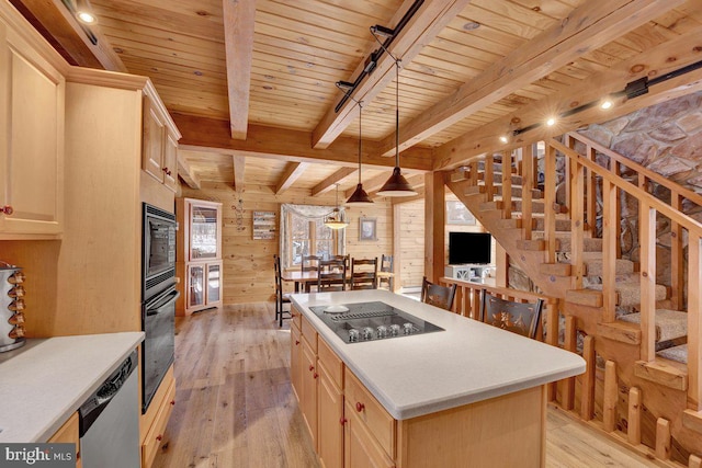 kitchen featuring light hardwood / wood-style flooring, wooden walls, a center island, black appliances, and decorative light fixtures