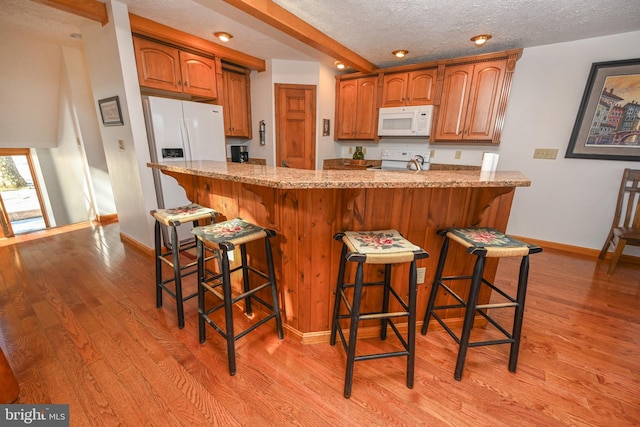 kitchen featuring white appliances, a kitchen breakfast bar, and light hardwood / wood-style floors