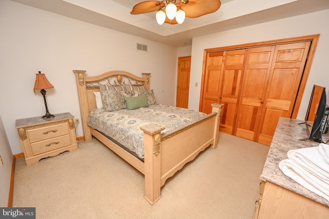 bedroom with ceiling fan, light colored carpet, a raised ceiling, and a closet