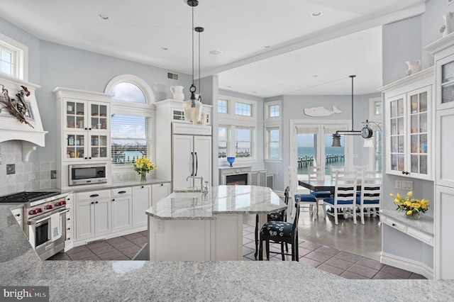 kitchen with high end appliances, dark tile patterned floors, pendant lighting, a kitchen island with sink, and white cabinets