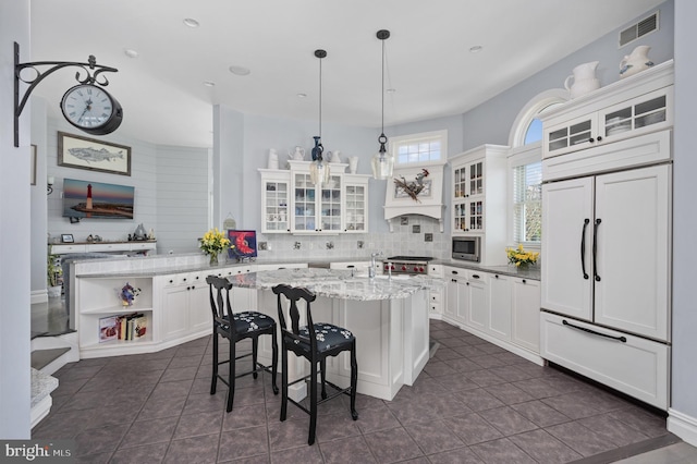 kitchen featuring light stone counters, decorative light fixtures, a center island, and white cabinets