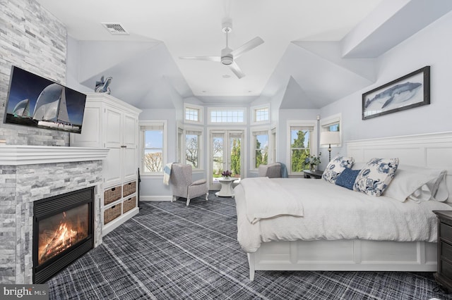 carpeted bedroom featuring a stone fireplace, vaulted ceiling, and ceiling fan