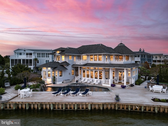 back house at dusk featuring a deck with water view and a balcony