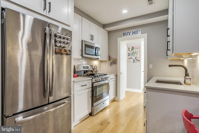 kitchen with sink, white cabinets, stainless steel appliances, light hardwood / wood-style floors, and backsplash