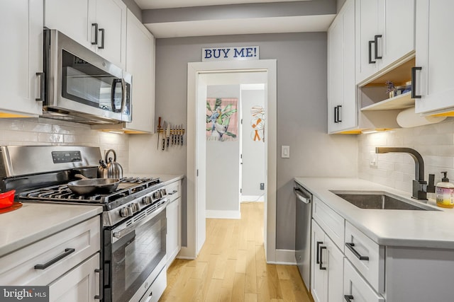 kitchen with sink, white cabinetry, stainless steel appliances, tasteful backsplash, and light hardwood / wood-style floors