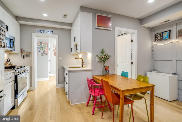 dining space with sink, light hardwood / wood-style flooring, and white cabinets