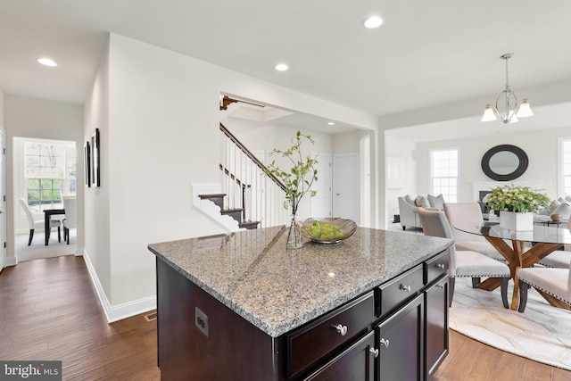 kitchen with an inviting chandelier, hanging light fixtures, dark hardwood / wood-style floors, a center island, and light stone counters