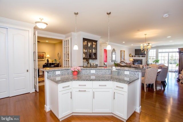 kitchen with light stone counters, hanging light fixtures, ornamental molding, hardwood / wood-style flooring, and white cabinets