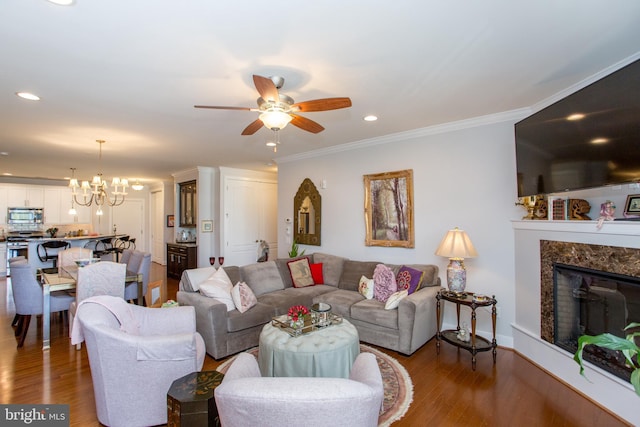 living room featuring hardwood / wood-style floors, ceiling fan with notable chandelier, a fireplace, and ornamental molding