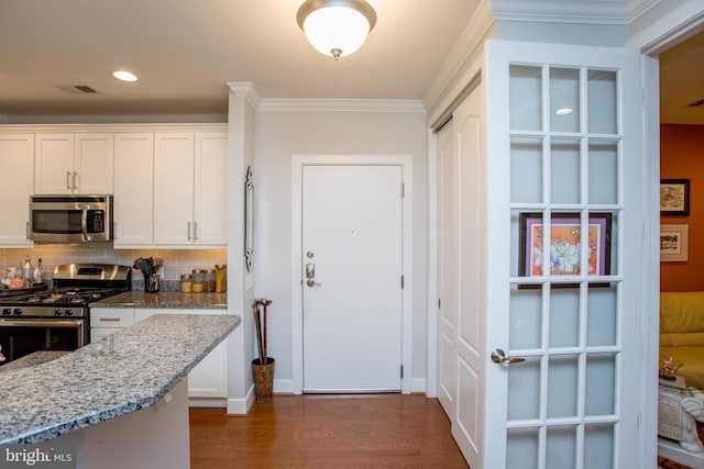 kitchen with crown molding, appliances with stainless steel finishes, white cabinetry, dark hardwood / wood-style floors, and light stone counters