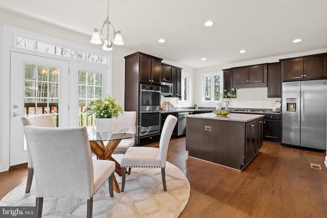 kitchen featuring appliances with stainless steel finishes, hanging light fixtures, hardwood / wood-style floors, dark brown cabinets, and a center island