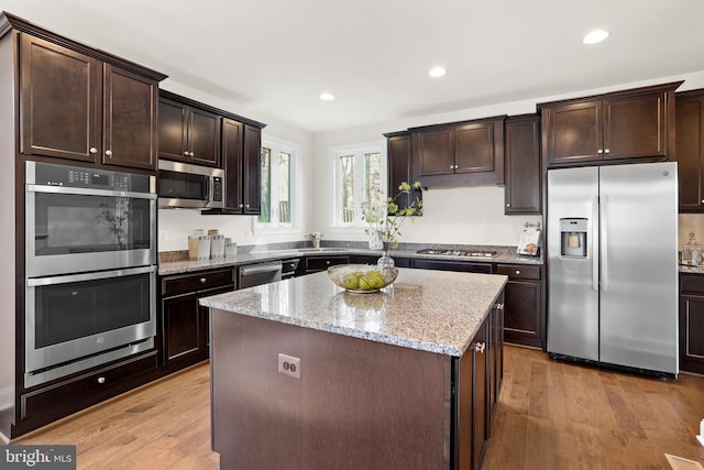 kitchen featuring dark brown cabinetry, a center island, appliances with stainless steel finishes, light stone countertops, and light hardwood / wood-style floors