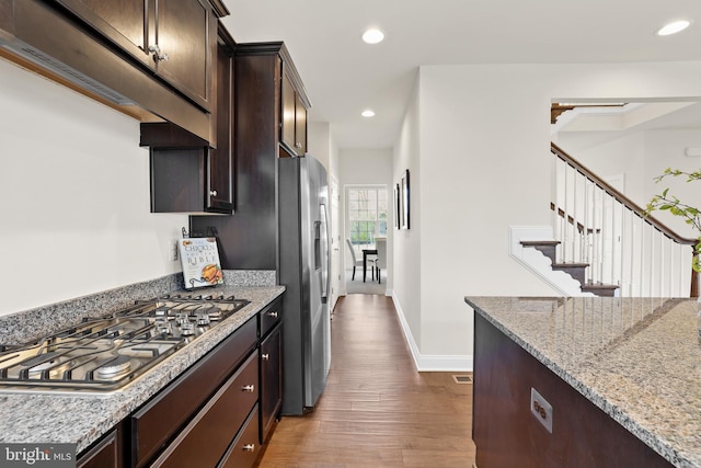 kitchen featuring light stone counters, dark brown cabinetry, appliances with stainless steel finishes, and wood-type flooring