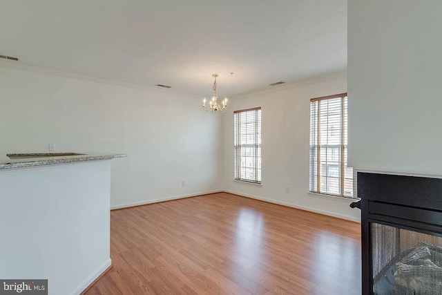 unfurnished living room with an inviting chandelier, a multi sided fireplace, ornamental molding, and light hardwood / wood-style flooring