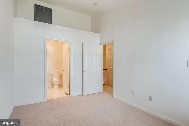 unfurnished bedroom with light carpet, ensuite bath, and a towering ceiling