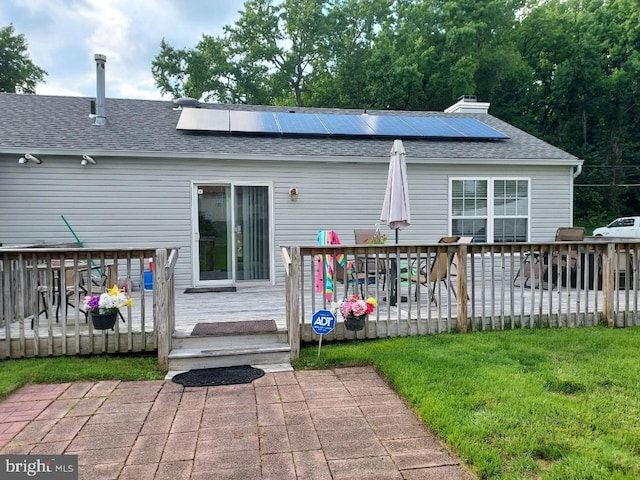 back of house with a wooden deck, a yard, and solar panels