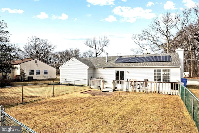 rear view of house featuring a deck, a lawn, and solar panels