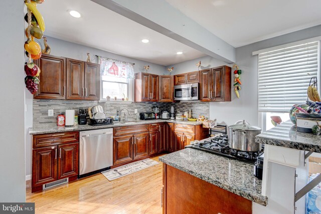 kitchen with appliances with stainless steel finishes, light stone countertops, light hardwood / wood-style flooring, and backsplash