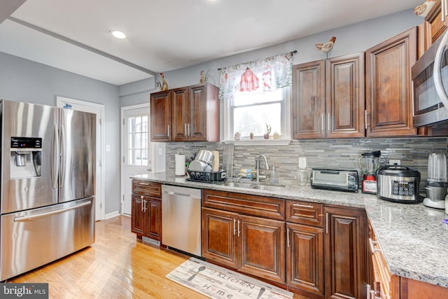 kitchen with sink, stainless steel appliances, light stone counters, tasteful backsplash, and light wood-type flooring