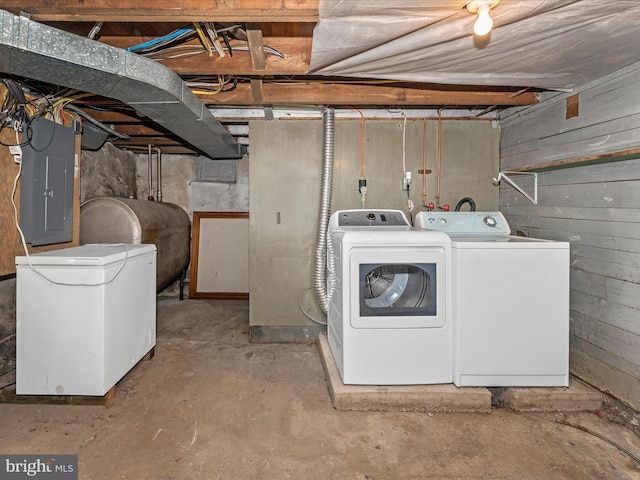 laundry room featuring separate washer and dryer, electric panel, and wood walls