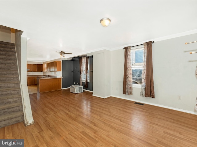 unfurnished living room with ceiling fan, ornamental molding, sink, and light wood-type flooring