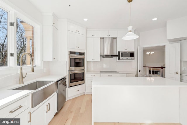 kitchen with a center island, appliances with stainless steel finishes, pendant lighting, wall chimney range hood, and white cabinets