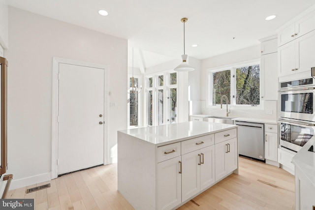 kitchen featuring sink, appliances with stainless steel finishes, white cabinetry, hanging light fixtures, and a kitchen island