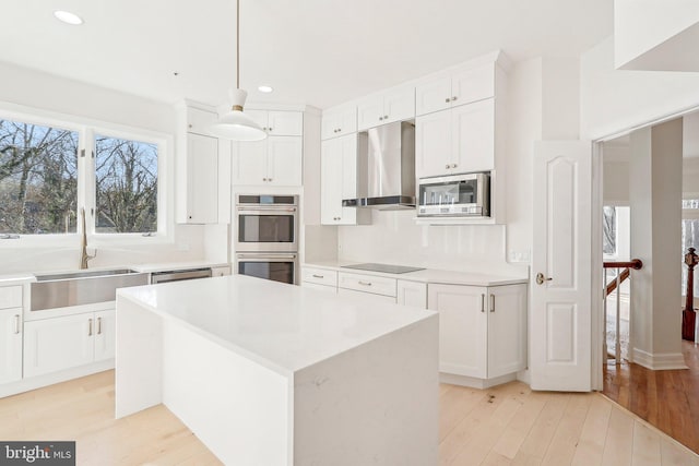 kitchen with a kitchen island, appliances with stainless steel finishes, decorative light fixtures, sink, and wall chimney exhaust hood